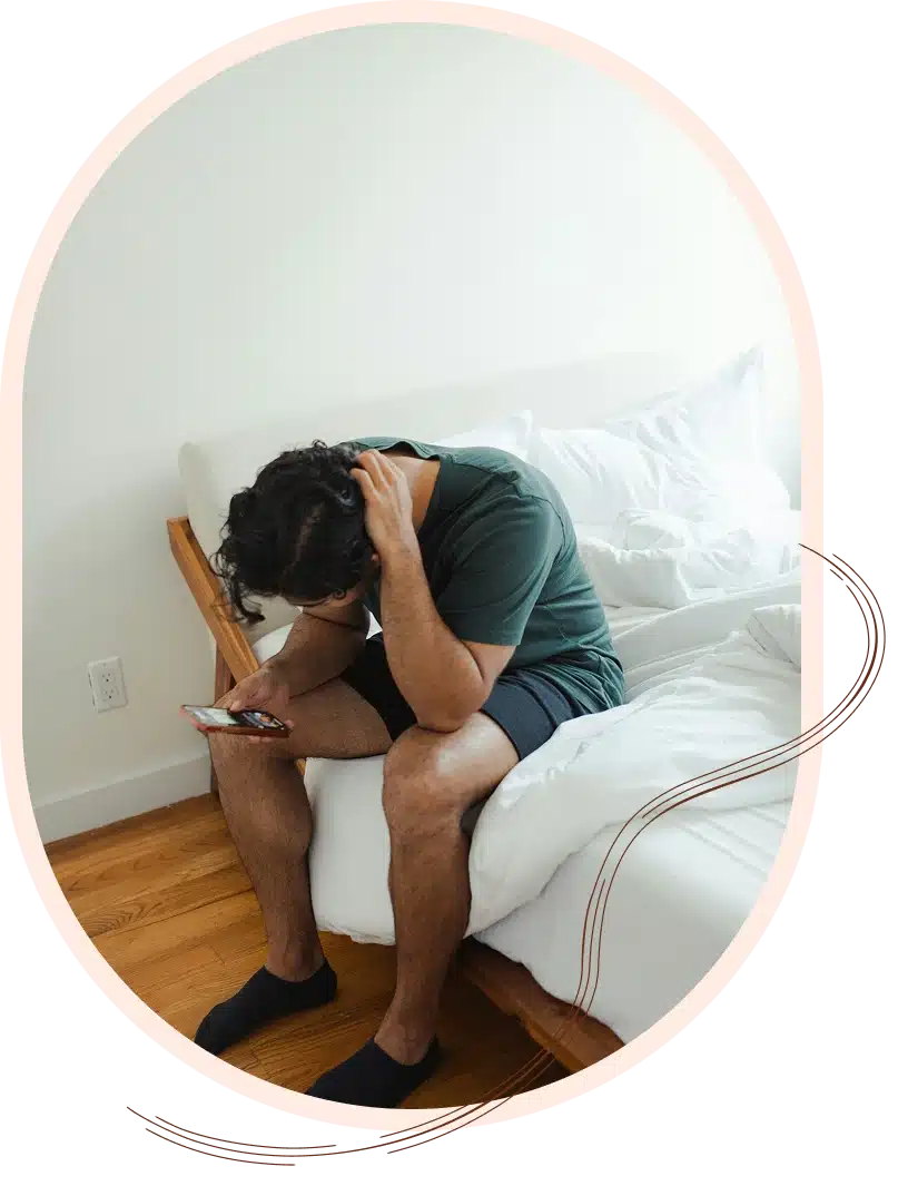 Person sitting on bed looking at phone with head in hand.