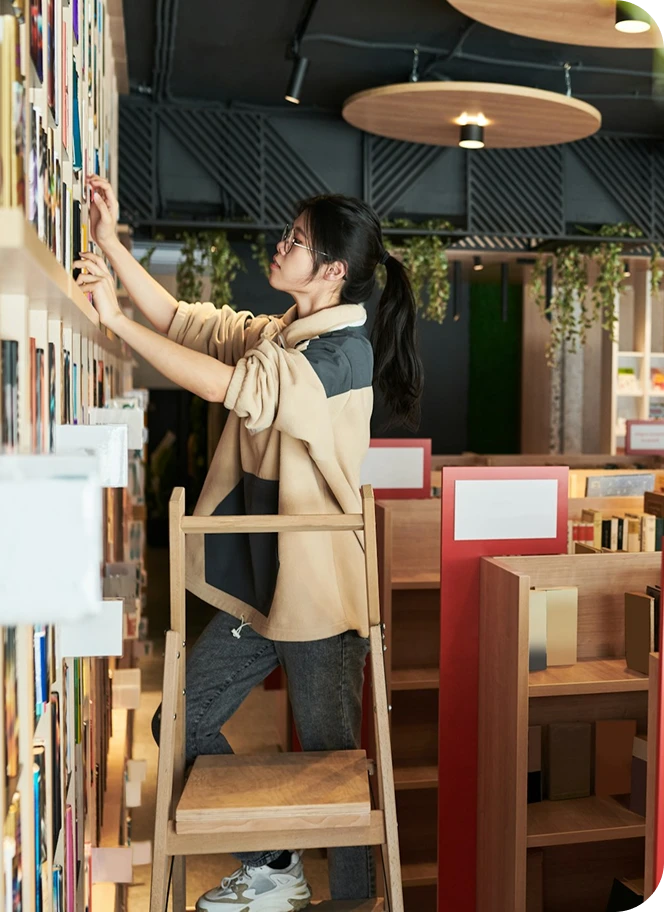 Woman organizing books on a high shelf.