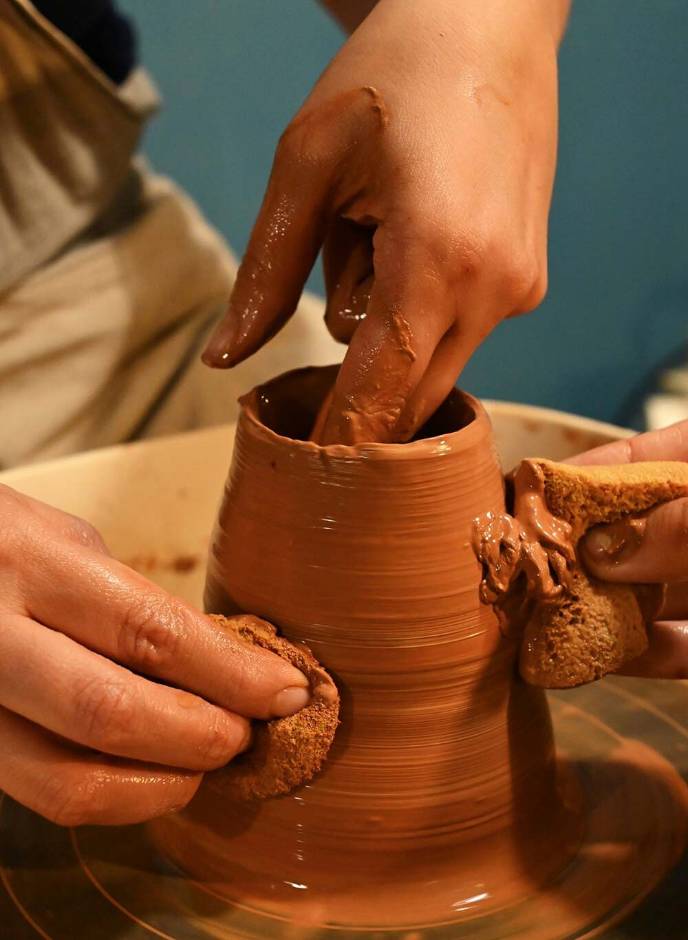 A potter's hands working on a clay pot on a pottery wheel.