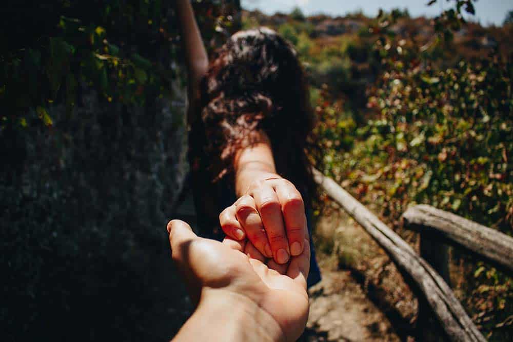 A hand reaching back to hold another person's hand on a dirt path