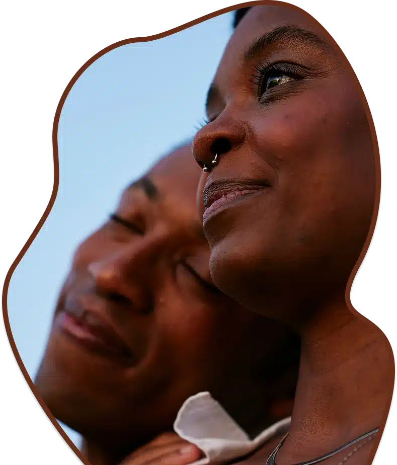 A close-up of a smiling woman looking up, with a man blurred in the background.