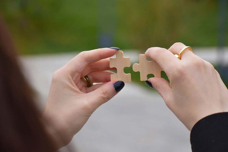 Hands connecting two wooden puzzle pieces.