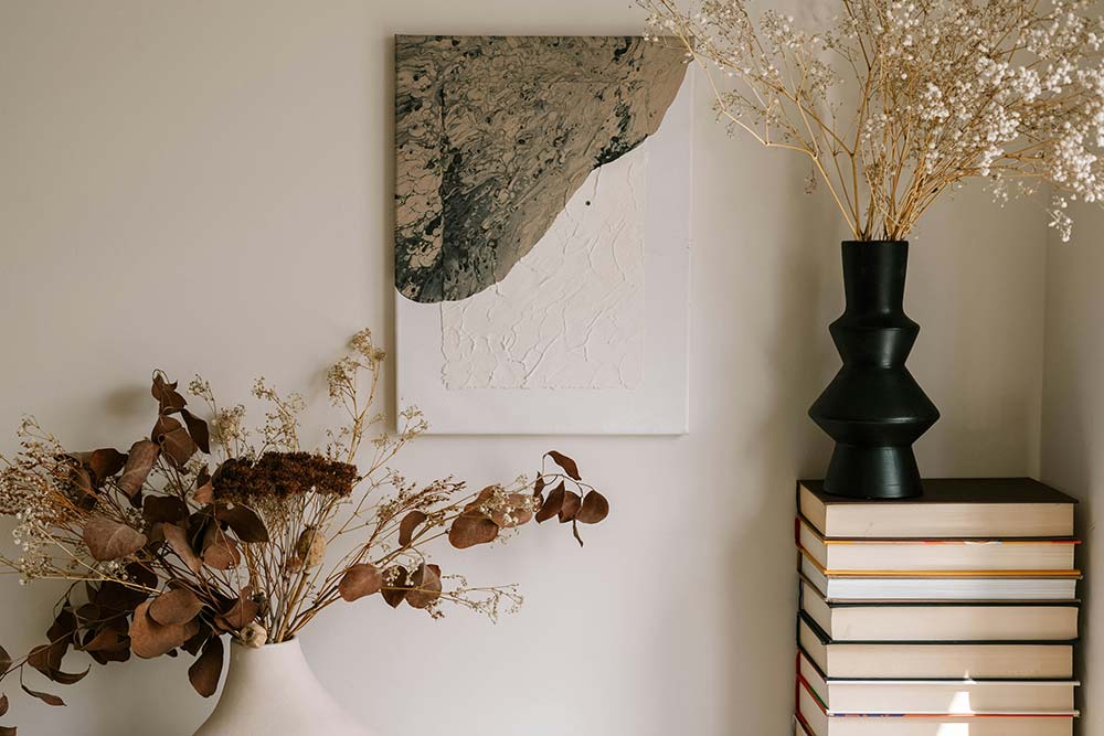 Interior still life with dried flowers, a stack of books, and abstract art.