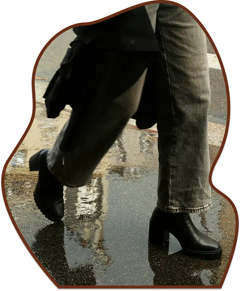 Low angle view of someone walking past a large puddle on a rainy city street, with buildings reflected in the water.