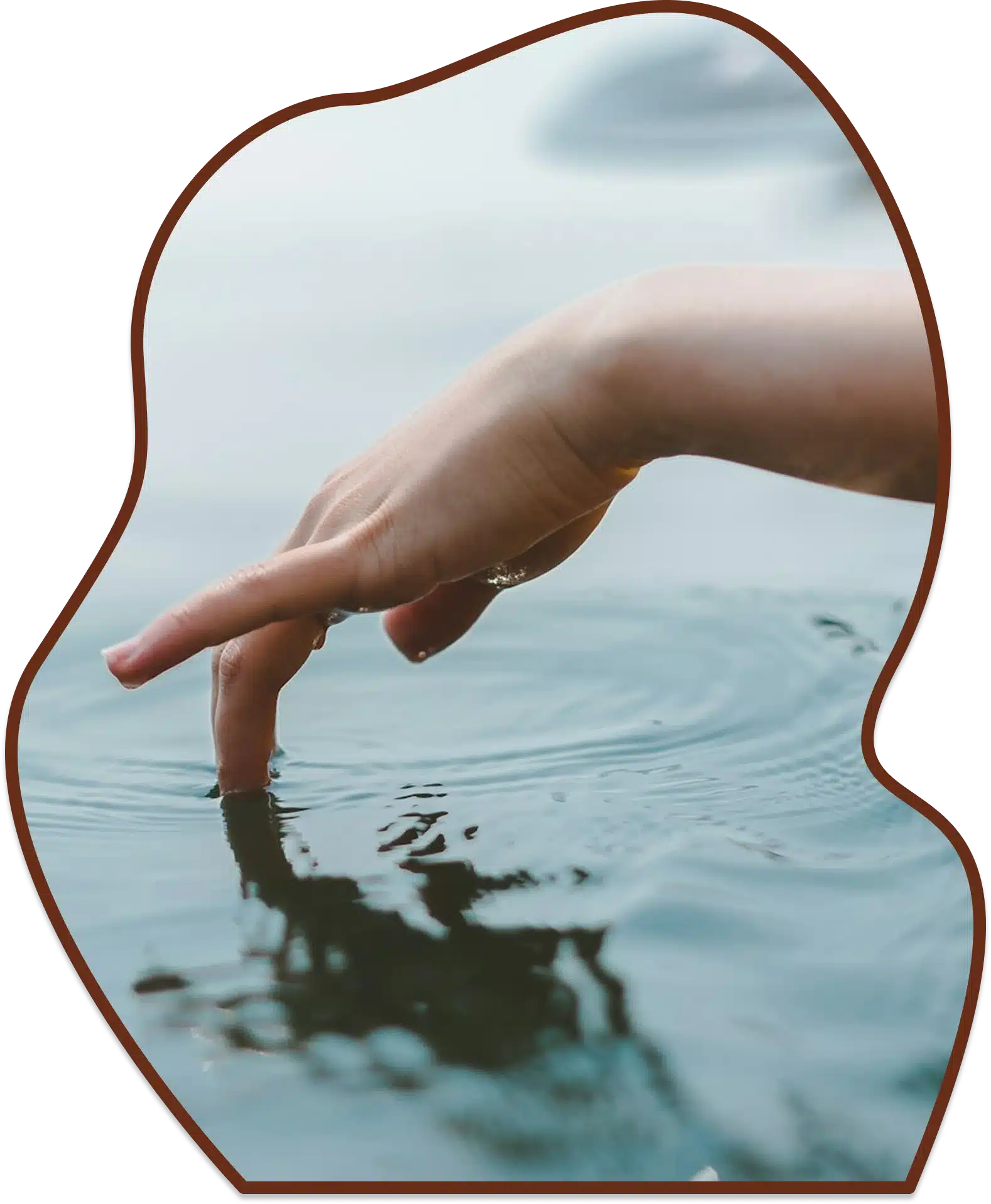 Close up of a hand dipping fingers into calm ocean water from the edge of a yellow kayak with a paddle behind it.